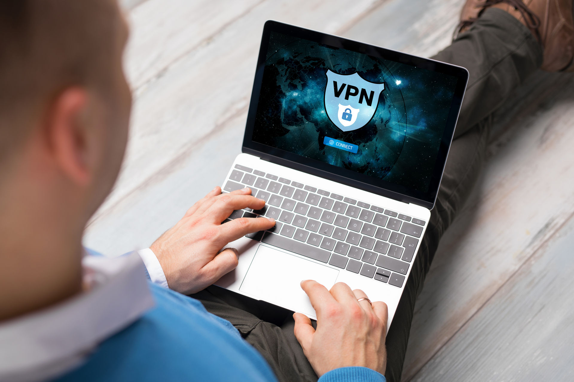 Osoba z laptopem na kolanach, na ekranie tarcza VPN i przycisk połączenia