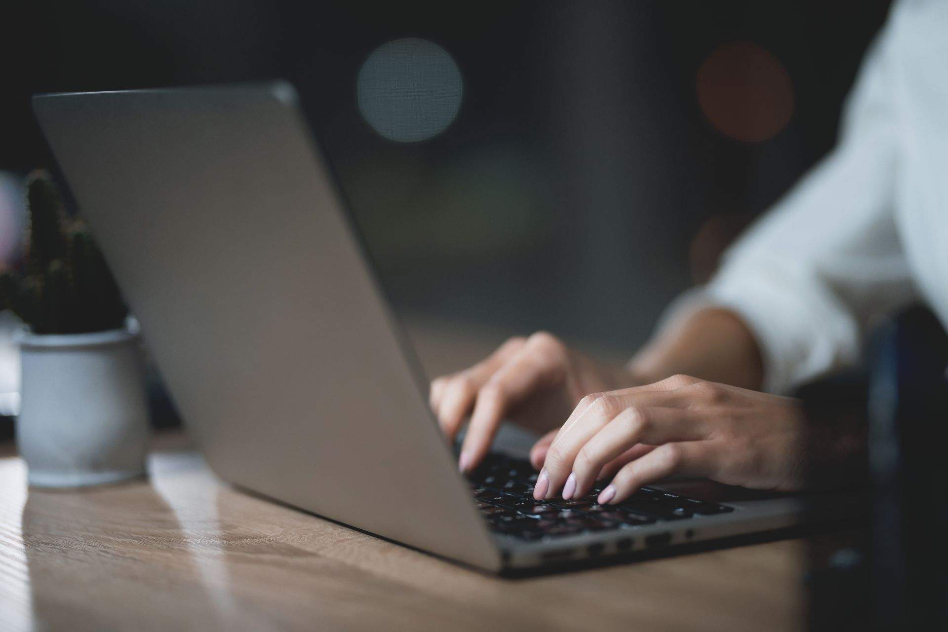 Dłonie piszące na klawiaturze laptopa przy biurku